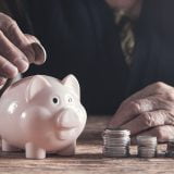 Elderly woman putting money to piggy bank.