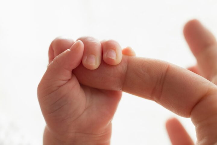 Close up baby hand gripping finger of father