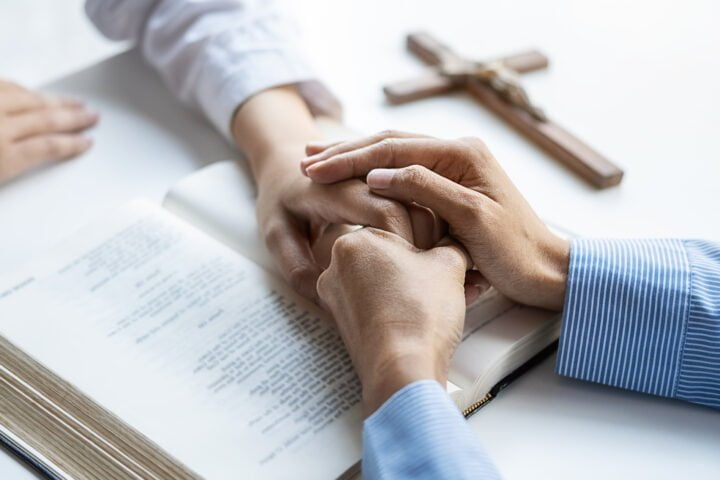 Christian woman praying with hands together on holy bible and wo