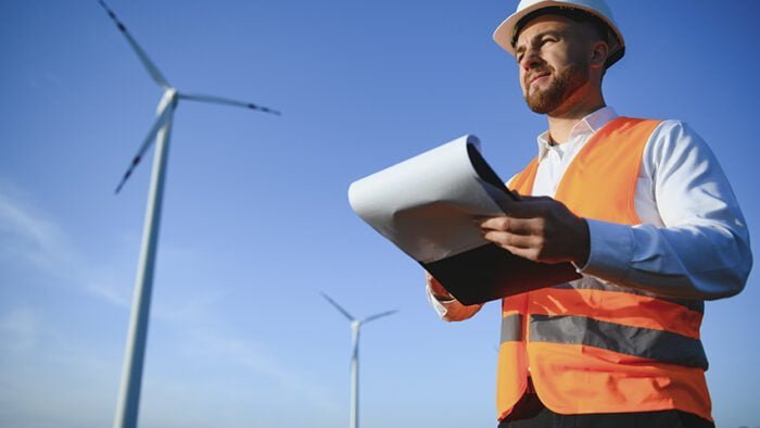 Engineer is checking energy production on wind turbine. Worker in windmills park in helmet.