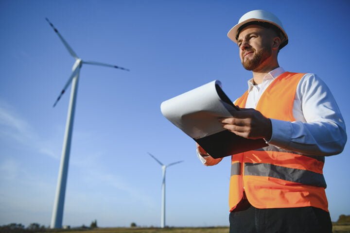 Engineer is checking energy production on wind turbine. Worker in windmills park in helmet.