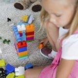 blurred girl in pink dress playing building blocks on carpet in kindergarten playroom