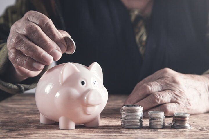 Elderly woman putting money to piggy bank.