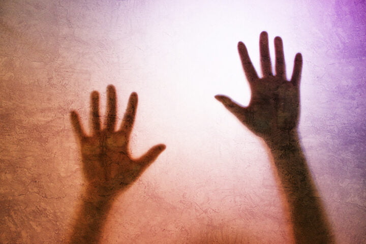 Captured person, back lit silhouette of hands behind matte glass