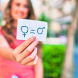 Young blonde girl smiling happy holding paper with gender equality concept walking at the city.