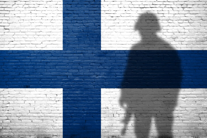 Flag of Finland painted on a brick wall with soldier shadow