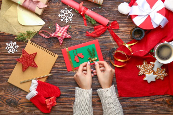 Woman decorating Christmas card  at wooden table