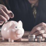 Elderly woman putting money to piggy bank.