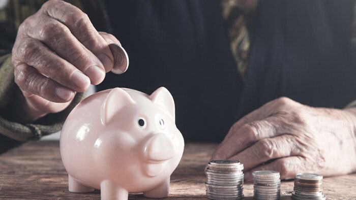 Elderly woman putting money to piggy bank.