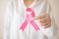 Breast Cancer Awareness Month in October. Close up of female in white shirt holding pink ribbon awareness for support people who live w/ breast cancer. Women's health care and medical concept.