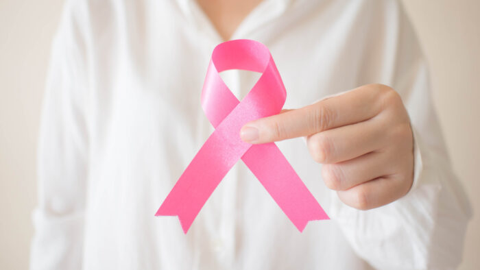 Breast Cancer Awareness Month in October. Close up of female in white shirt holding pink ribbon awareness for support people who live w/ breast cancer. Women's health care and medical concept.