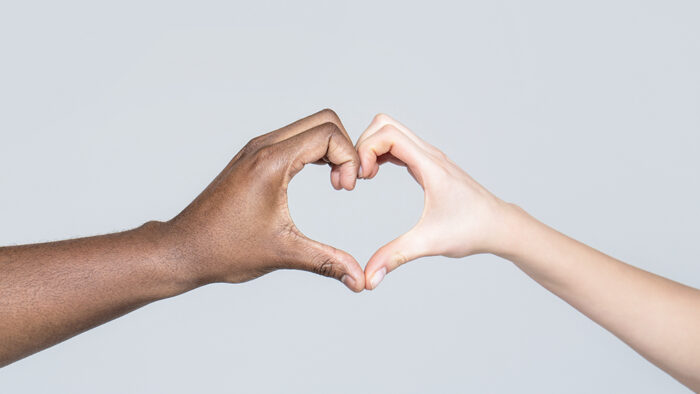People different skin colors put their hands together making heart shape in white background. Charity, love and diversity - closeup of female and male hands of different skin color making