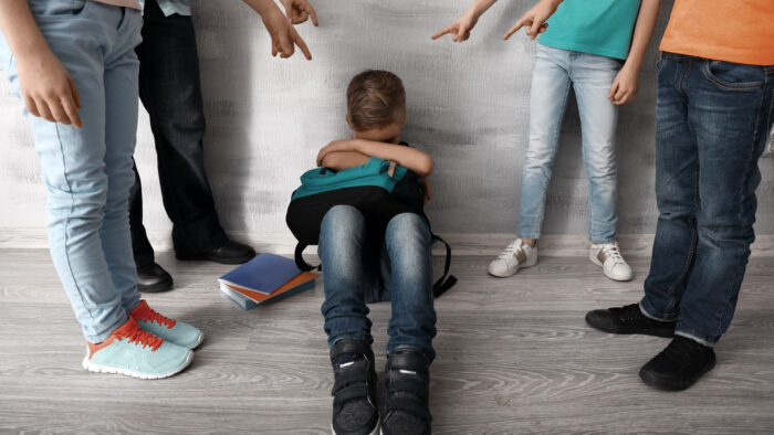 Children bullying little boy with backpack indoors