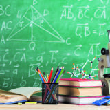 Education and sciences concept - books, molecule model and microscope on the desk in the auditorium, chalkboard background.