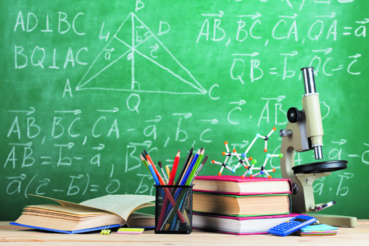 Education and sciences concept - books, molecule model and microscope on the desk in the auditorium, chalkboard background.