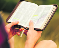 Reading the Bible outdoors in nature. A man in sunglasses and a shlap holds a Bible in his hands